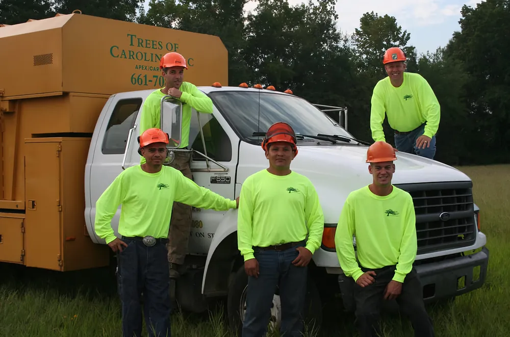 Trees of Carolina crew in hi-vis shirts and helmets beside a branded chip truck