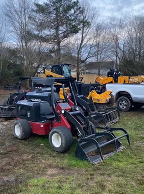 Red compact loaders with grapple attachments and yellow equipment in the yard